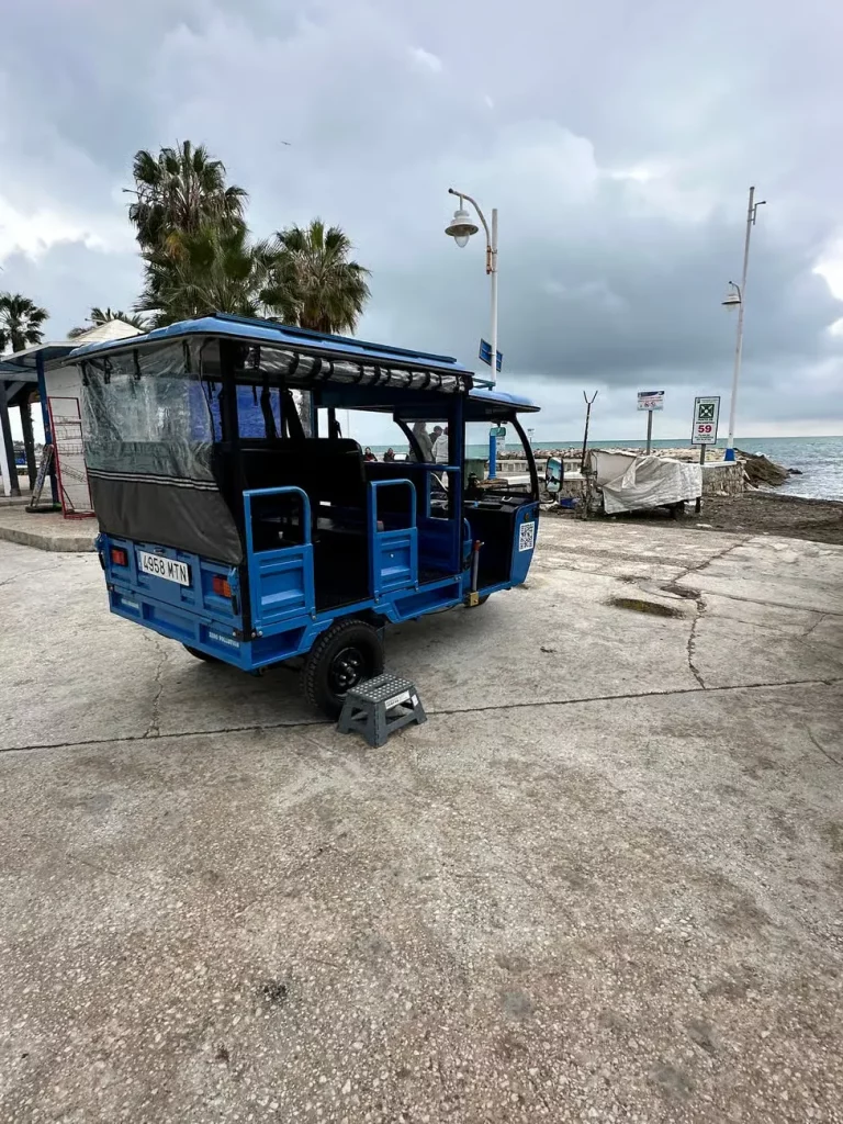 Tuk tuk azul vacío aparcado en un paseo marítimo bajo un cielo nublado
