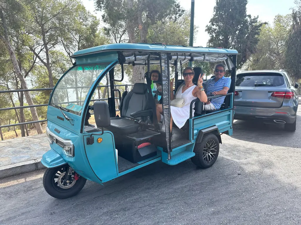 Tuk tuk turquesa de Baloo-Go con pasajeras saludando, aparcado en un mirador entre pinos